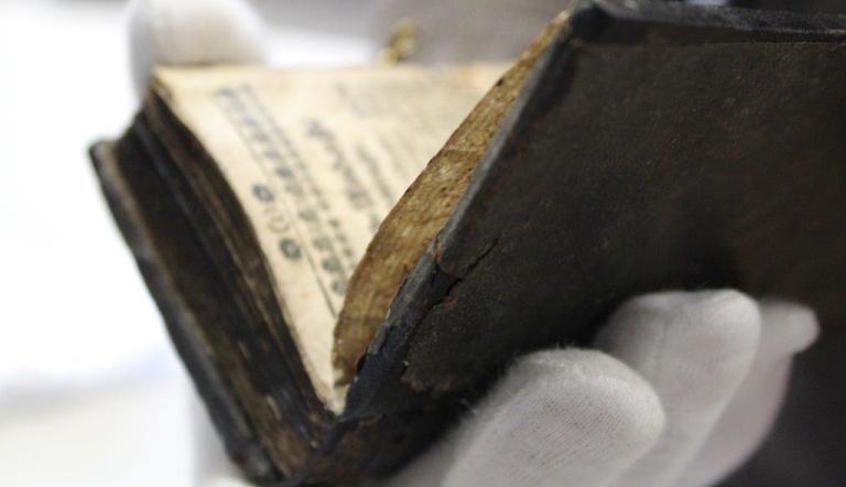 Aus dem Depot des Potsdam Museums eine Hand mit Archivarhandschuh hält ein altes buch in der Hand