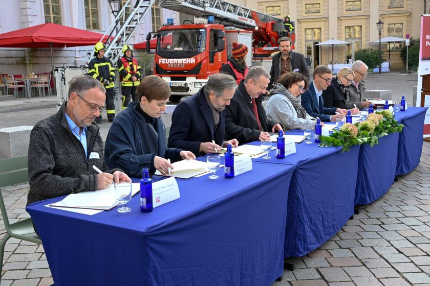 Unterzeichnende sitzen an einem Tisch auf dem alten Markt